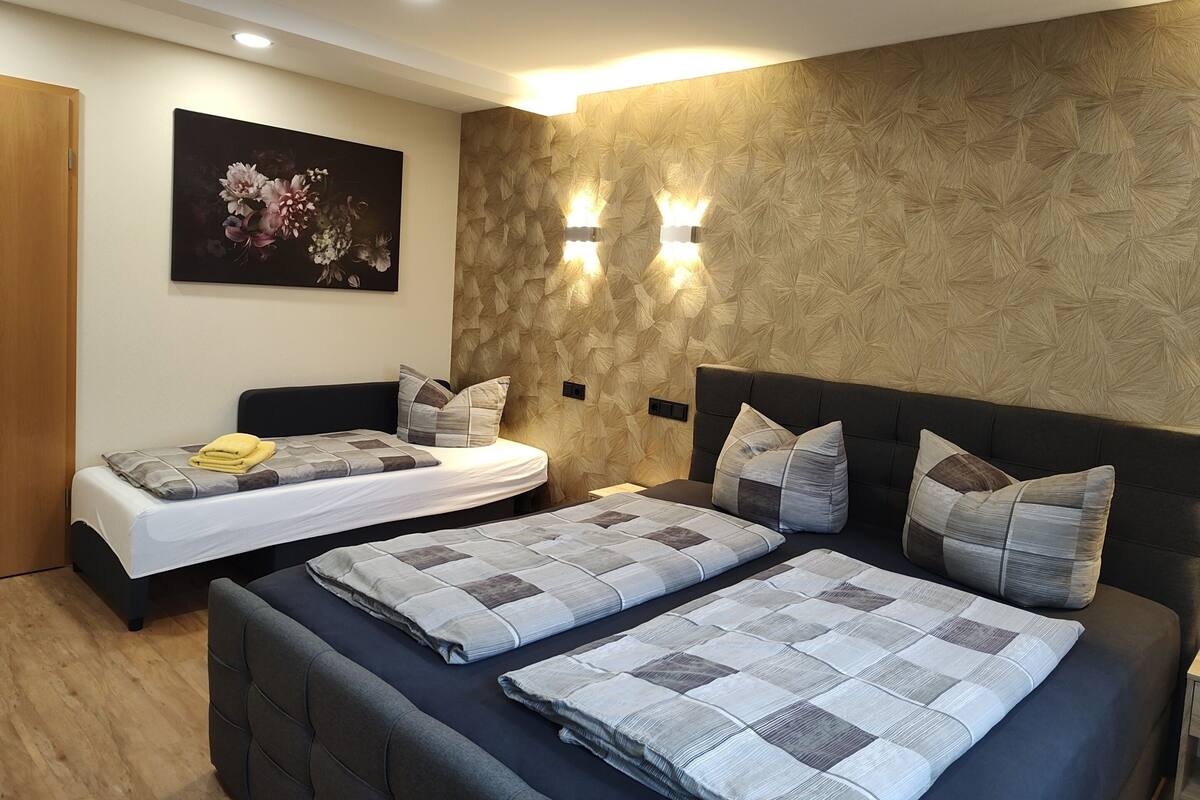 A modern bedroom with two beds, a large painting, and wall-mounted lighting.