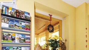 Una habitación con una pared amarilla, una ventana adornada con una guirnalda, una estantería con folletos turísticos y una pequeña decoración de casa.