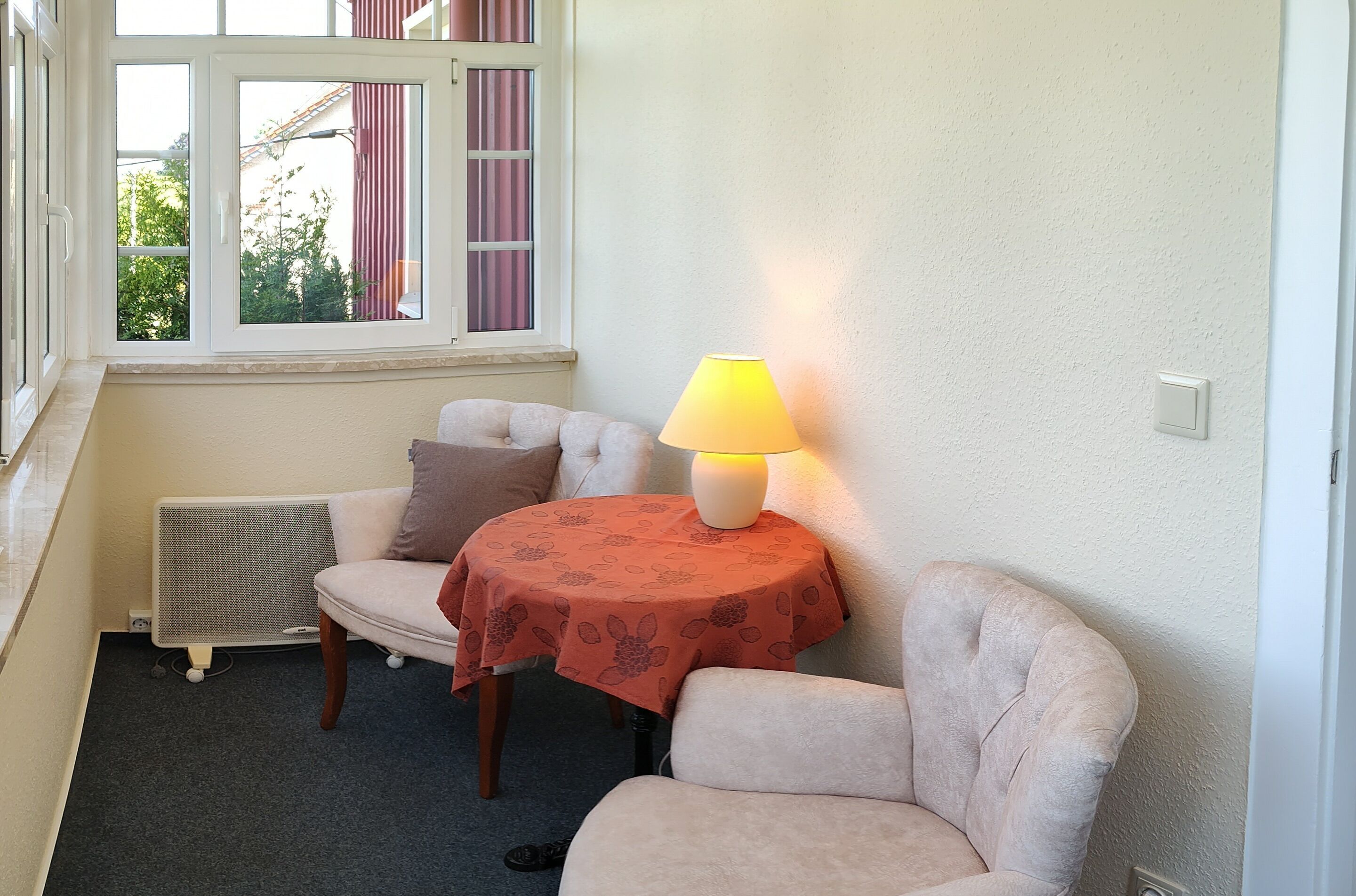 Una habitación acogedora con ventana, una mesa con lámpara y dos sillas.