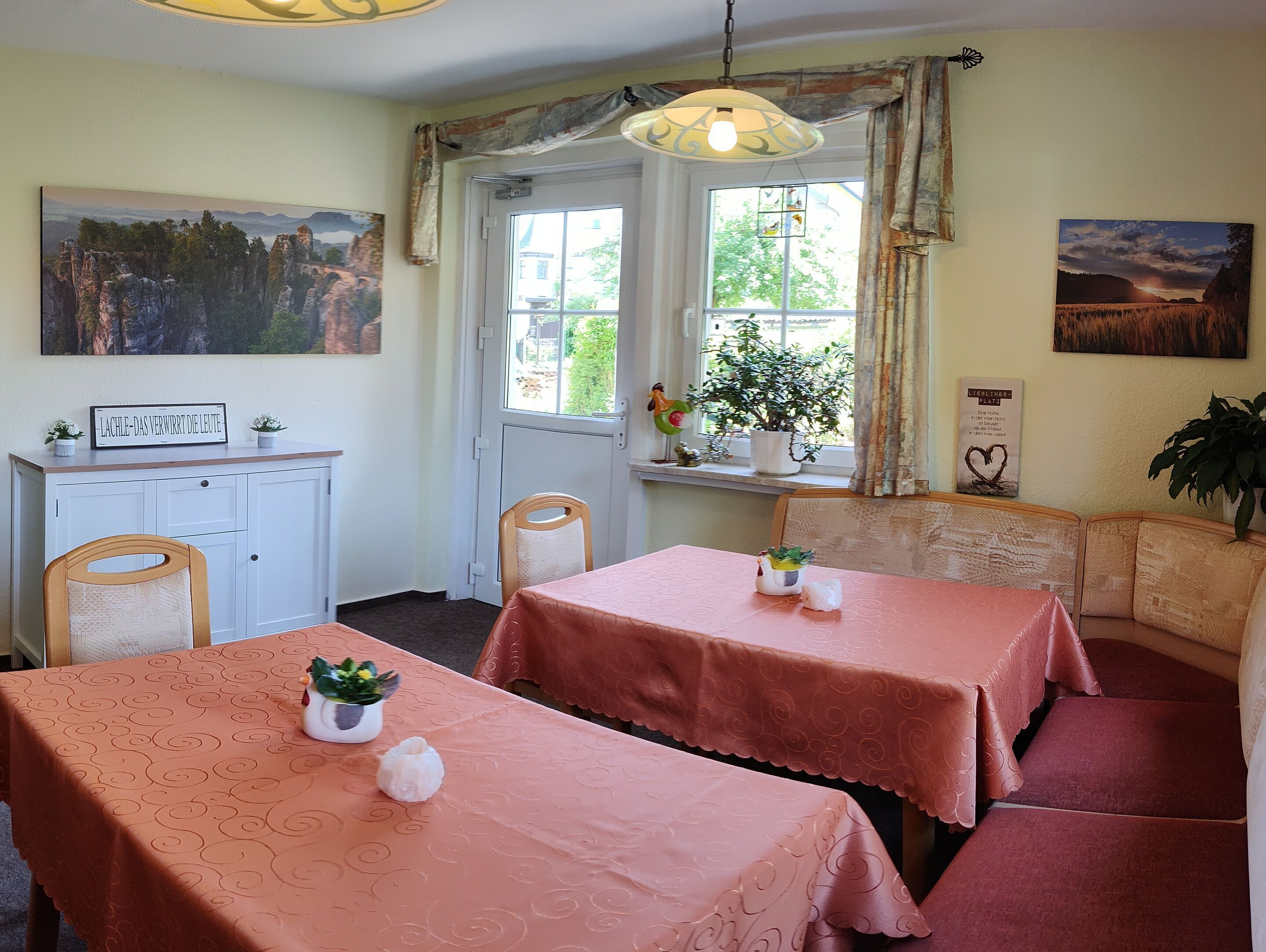 A dining area with two tables, chairs, a bench, a window with curtains, a cabinet, and wall art.