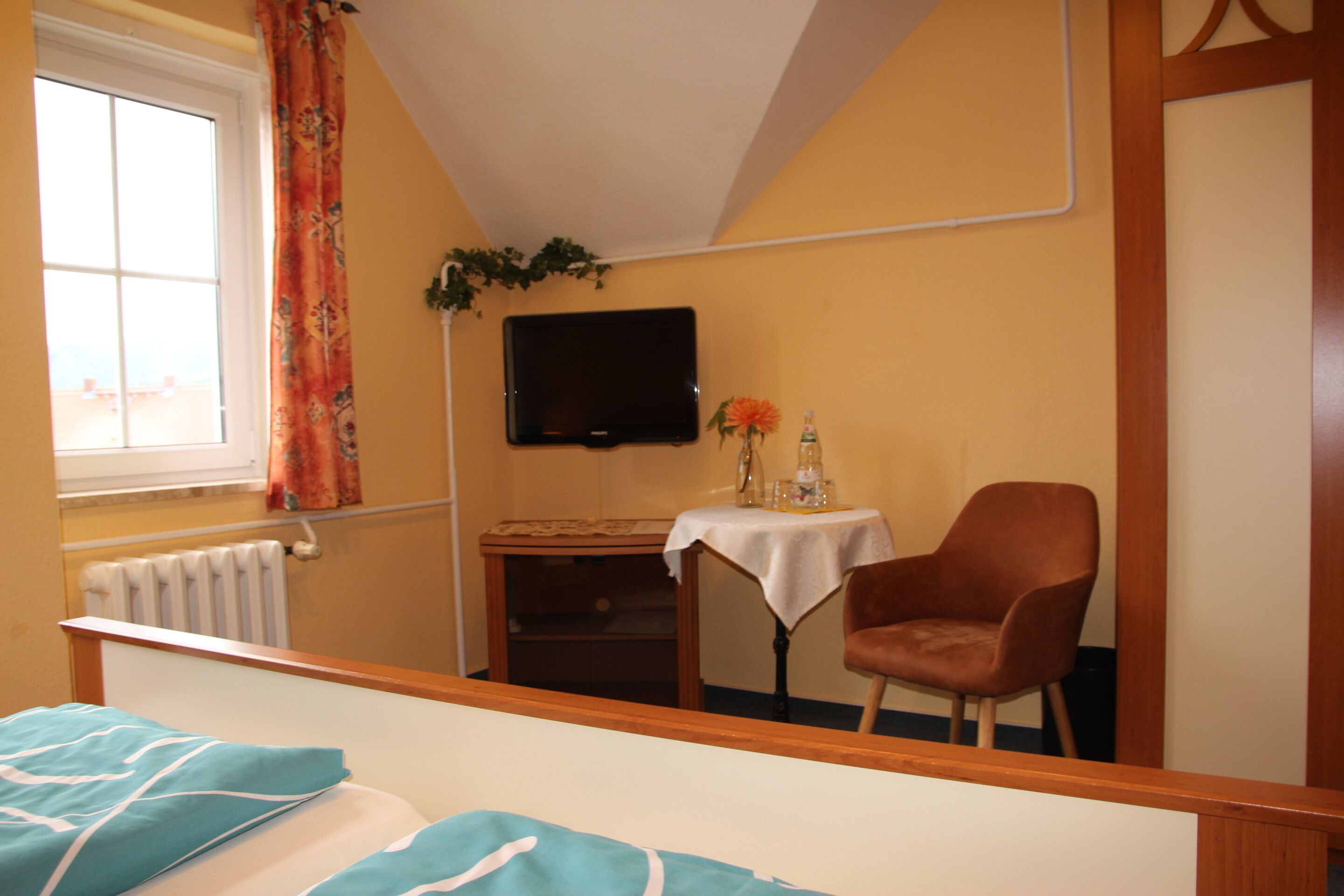 Una camera d'albergo con un letto, una televisione, un tavolino con una sedia, una finestra con tende e un termosifone.