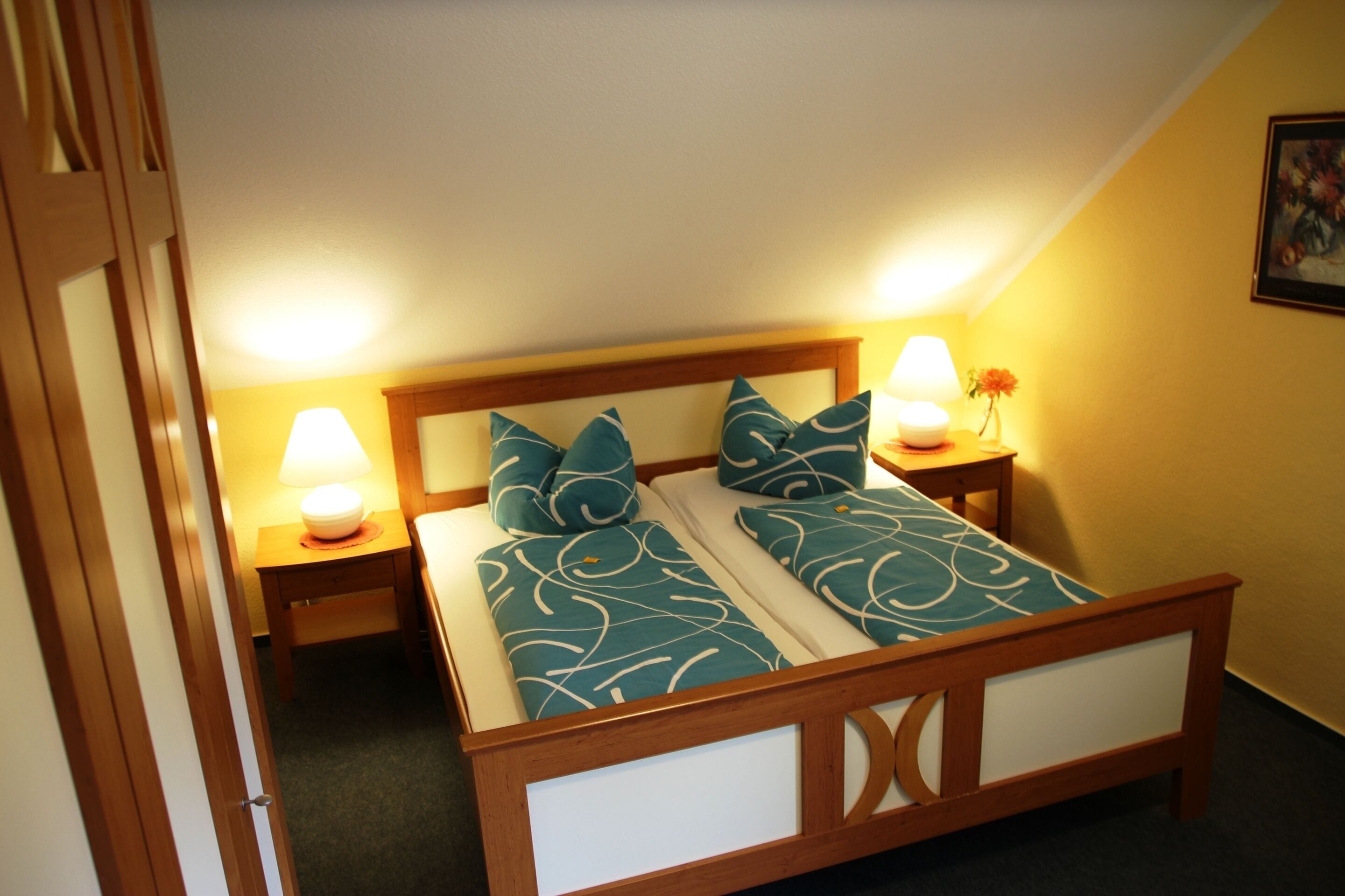 A bedroom with a wooden bed frame, two bedside lamps, and a nightstand with a vase of flowers.