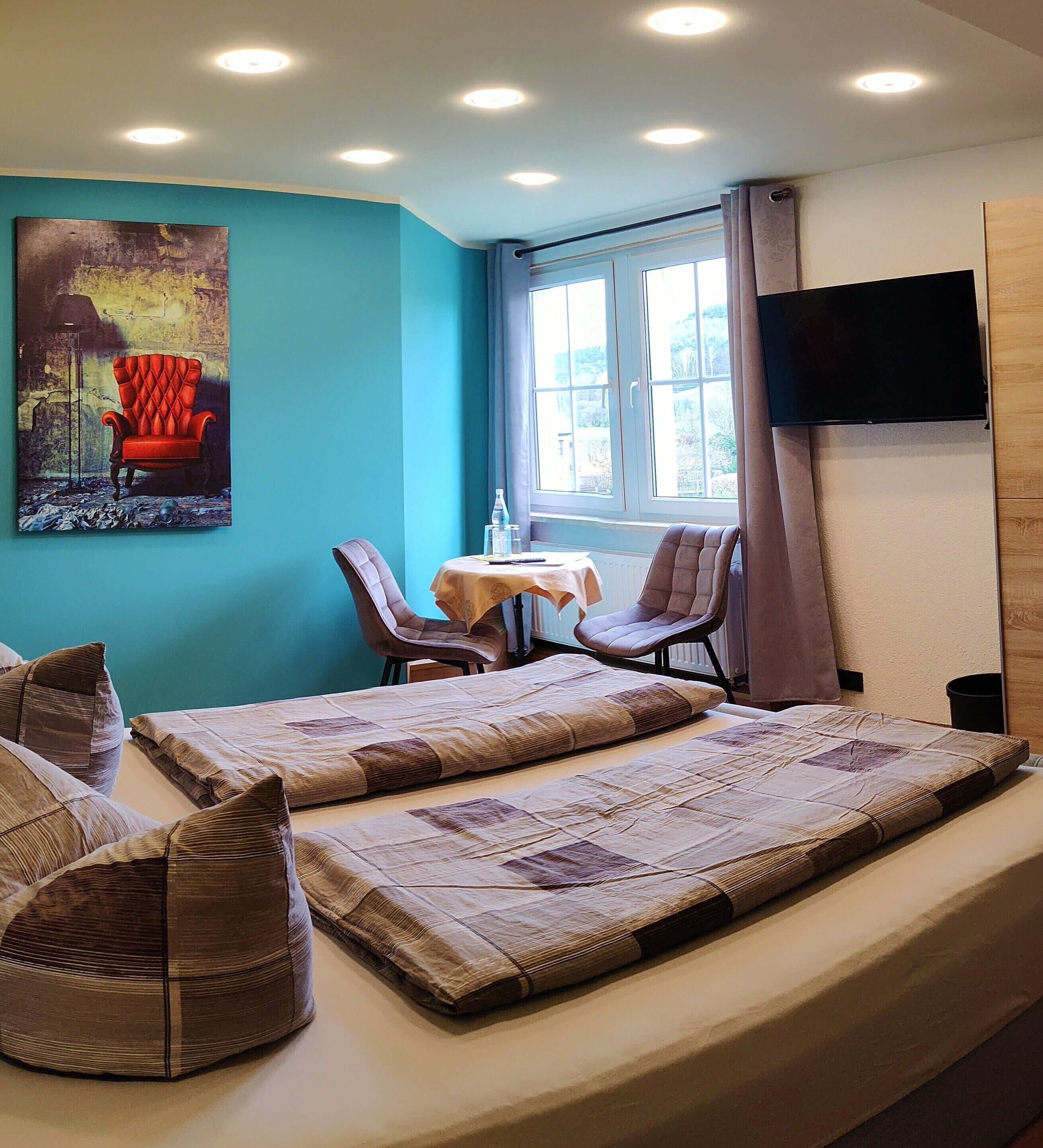 A hotel room with a bed, a desk, two chairs, a TV, and a window with curtains.