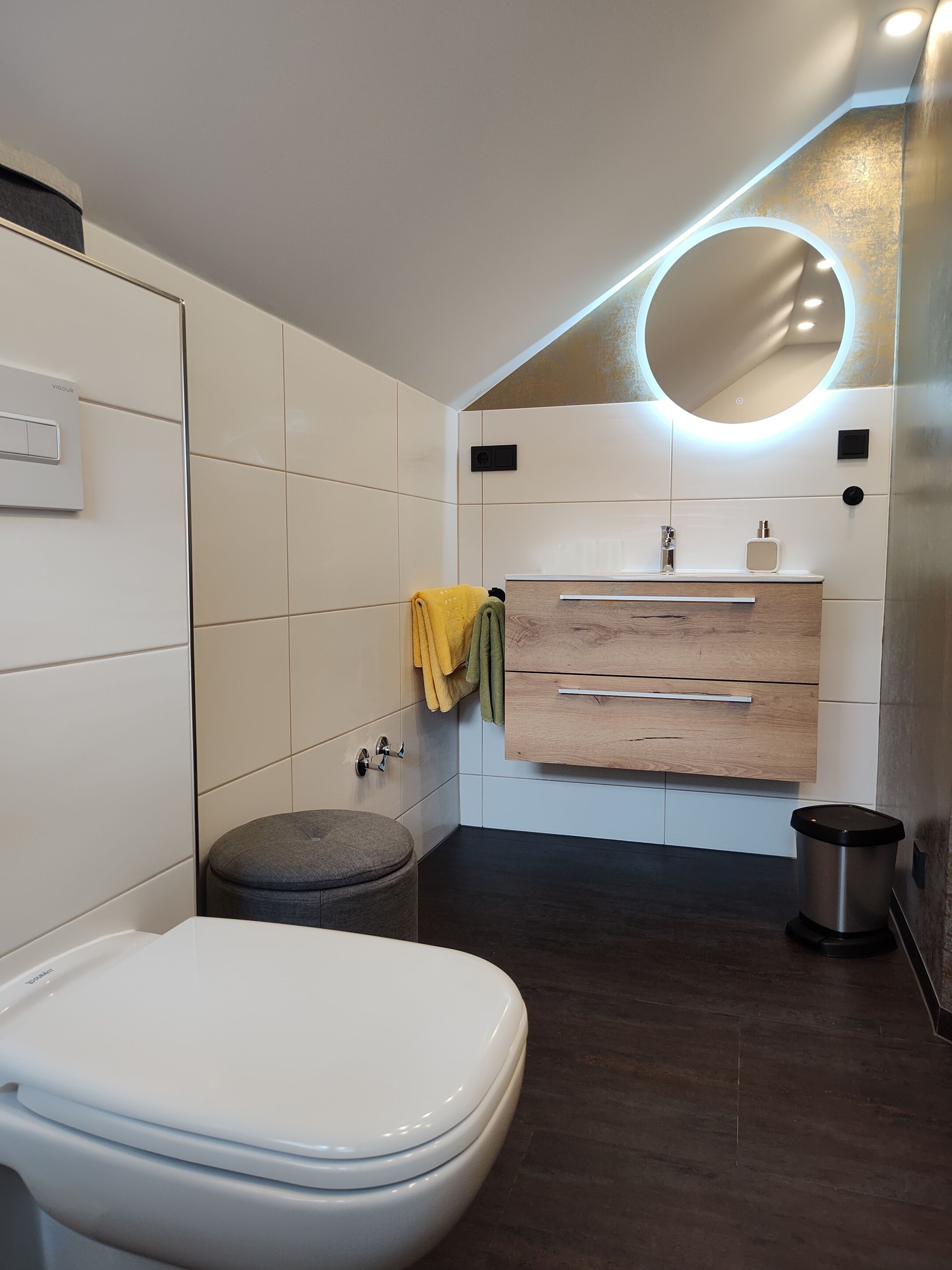 A modern bathroom with a white toilet, a wooden vanity with a mirror, and a small stool.