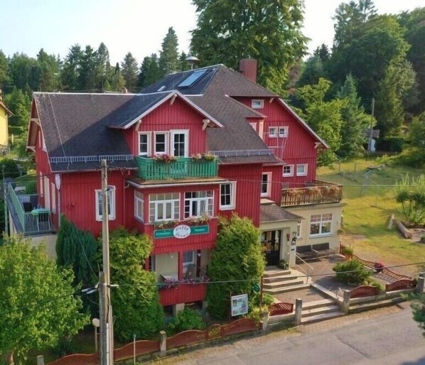 Una casa roja de dos pisos con un balcón, un letrero visible y un pequeño porche.