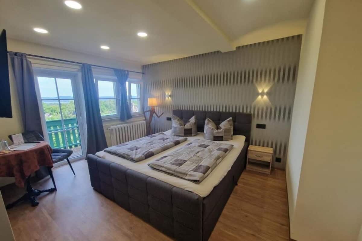 A bedroom with a large bed, a small table, and a view of greenery through the window.