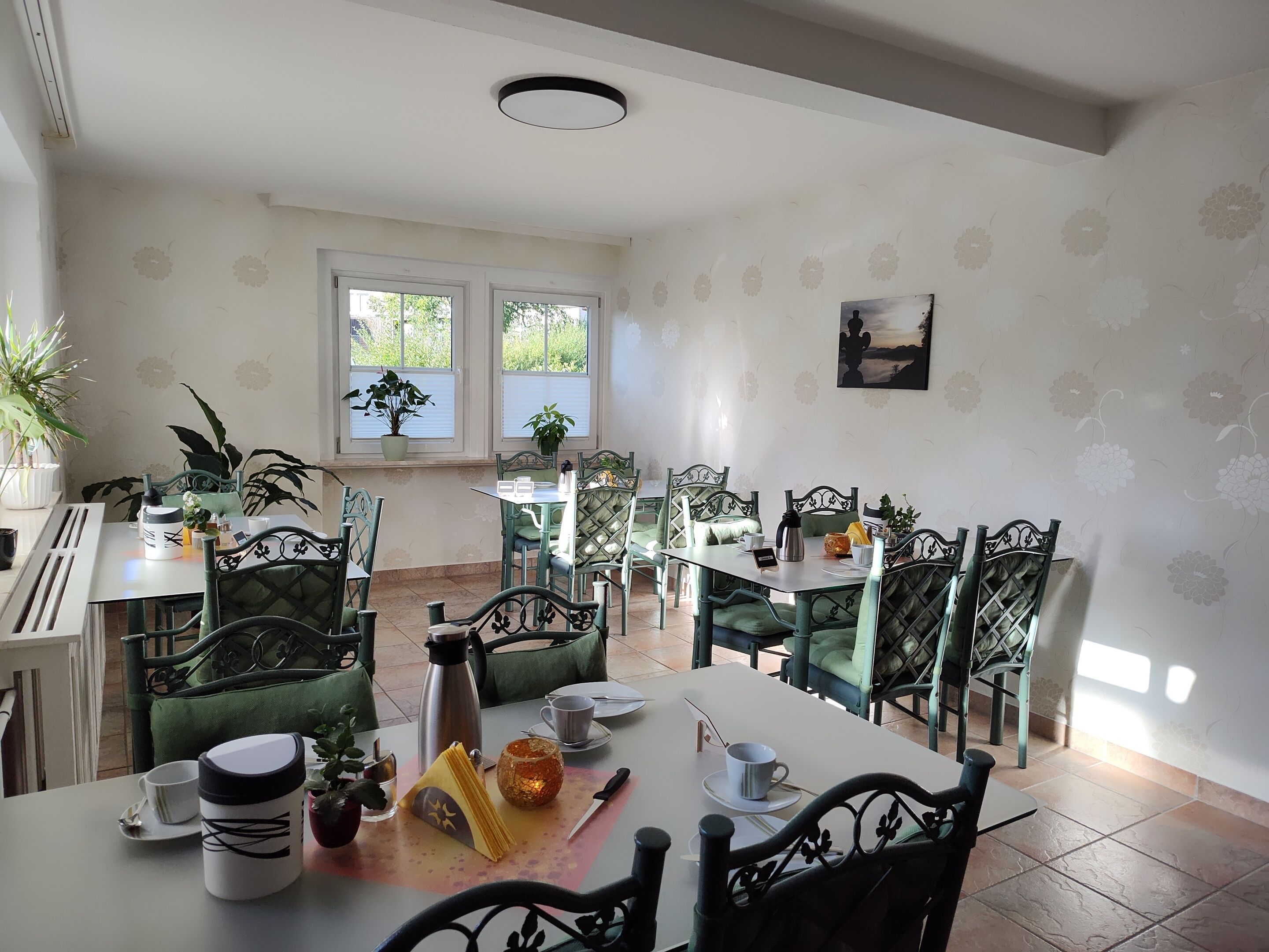 A dining area with green upholstered chairs, white tables, and potted plants.