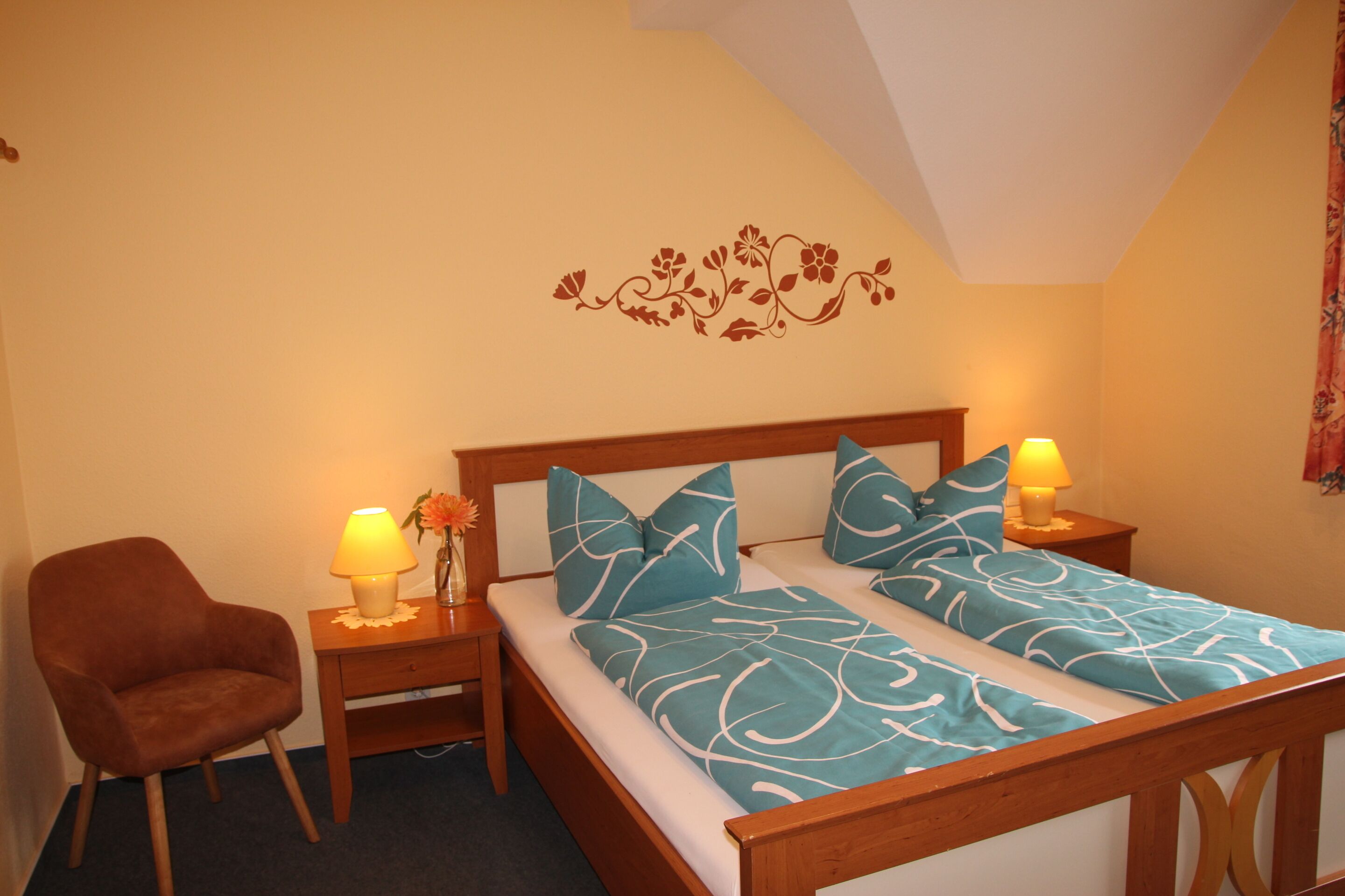 A bedroom with a wooden bed, two nightstands with lamps, a chair, and a floral wall decal.