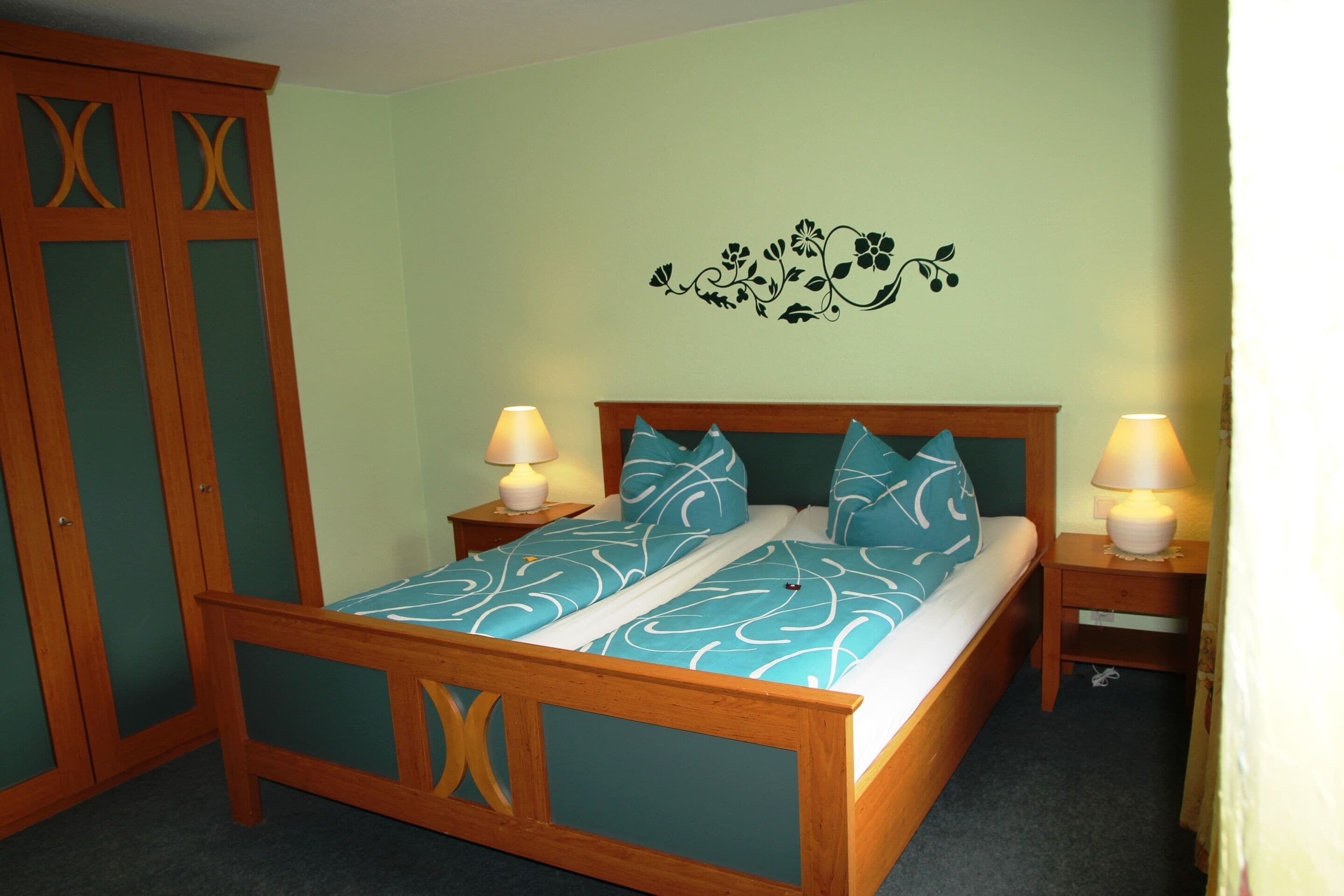 Een slaapkamer met een houten bed, twee nachtkastjes met lampen, een kledingkast en een bloemenstickerset op de muur.