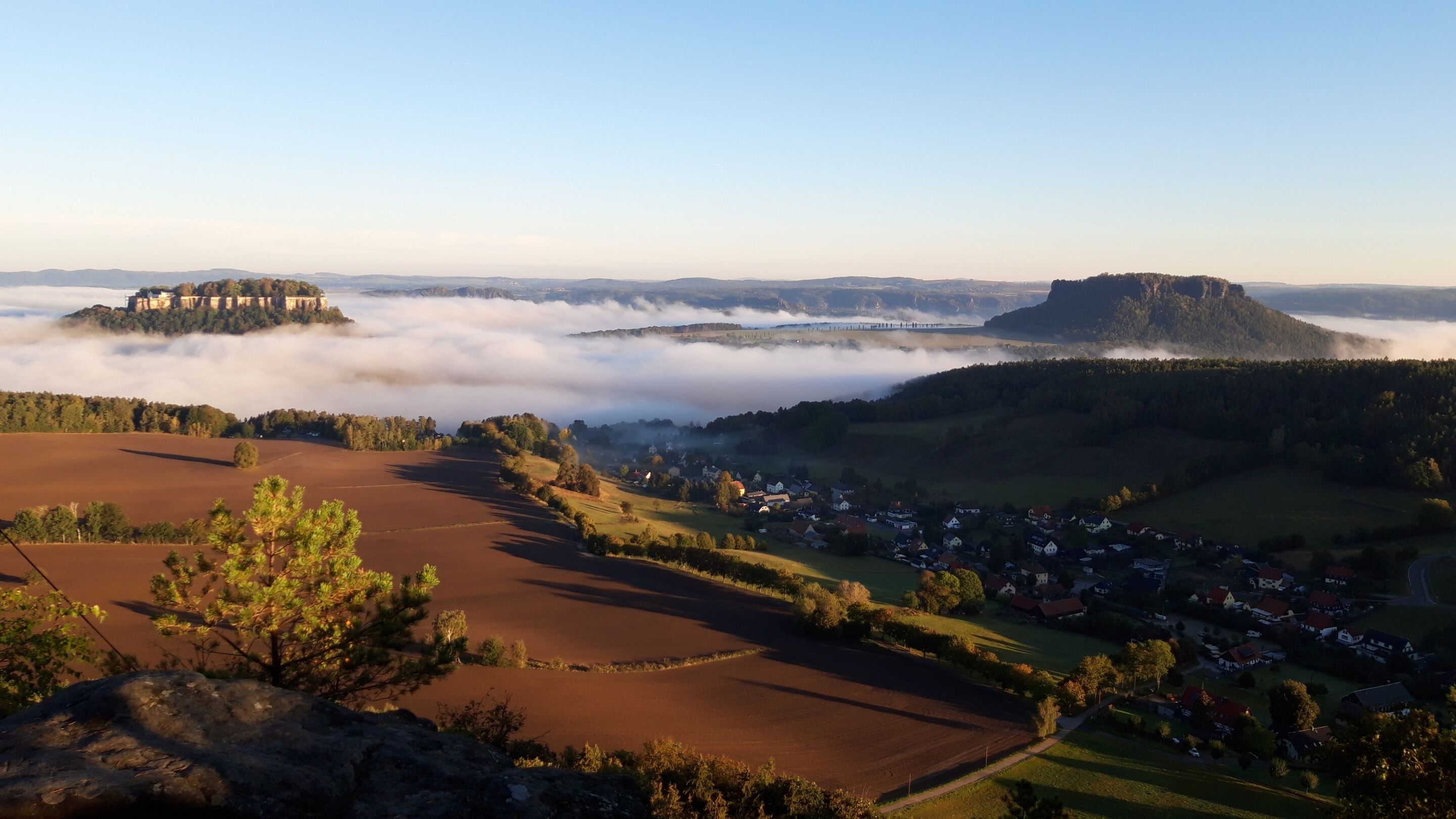 Vista panorámica de un pueblo con un castillo en una colina, rodeado de campos y un área boscosa.