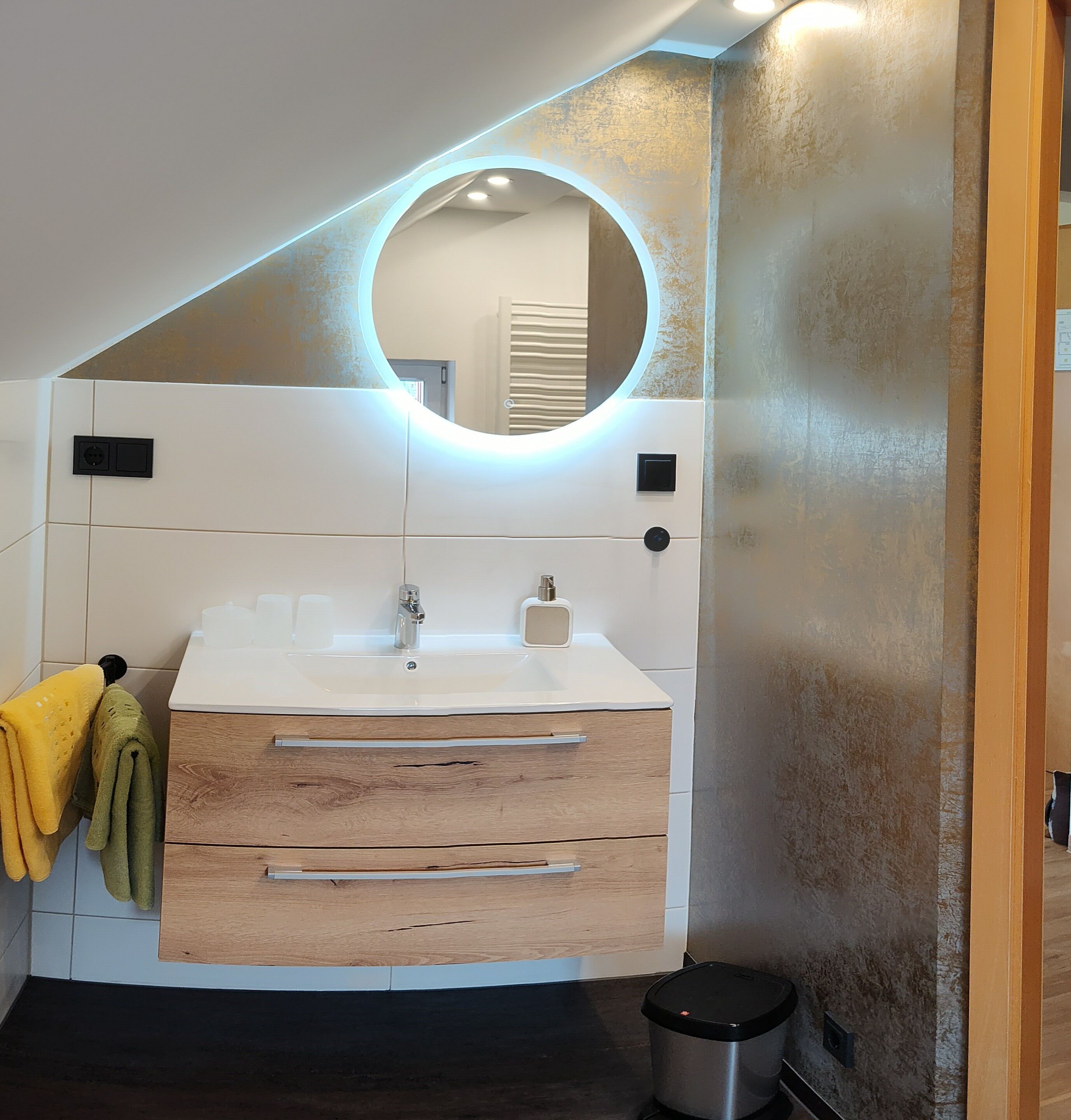Ein modernes Badezimmer mit einem weißen Waschtisch, einem runden Spiegel und einem Holzschrank.
