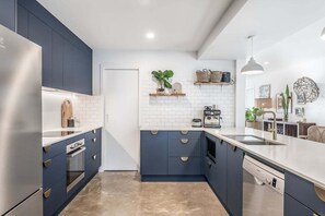 A modern kitchen with dark blue cabinets, white countertops, and stainless steel appliances.