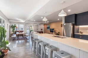 A modern kitchen with a central island, bar stools, and a stainless steel refrigerator. - Salty Crab Bungalow - short walk to the beach (Lennox Head)