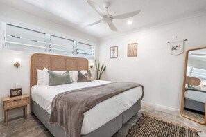 A bedroom with a bed, bedside table, wall-mounted light, ceiling fan, and a mirror. - Salty Crab Bungalow - short walk to the beach (Lennox Head)