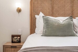 A bed with a woven headboard, a bedside table with a picture frame, and a wall-mounted light fixture.