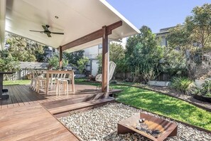 An outdoor patio with a wooden deck, a table with chairs, a fire pit, and a covered seating area with a ceiling fan.