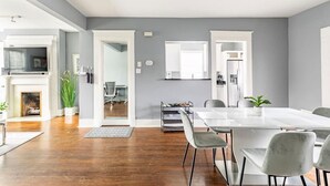 A modern kitchen with a built-in oven, a dining area with a white table and chairs, and a grey wall with a mirror. - 2 BR • Oak Lawn House by Uptown • WFH Setups (Dallas)