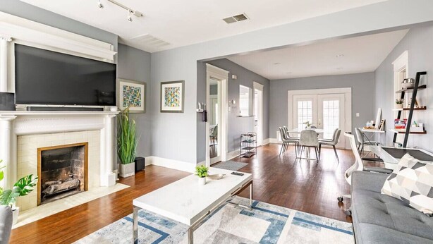 A modern living room with a fireplace, a flat-screen TV, and a dining area with a table and chairs. - 2 BR • Oak Lawn House by Uptown • WFH Setups (Dallas)