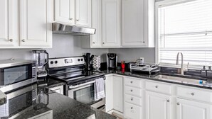 A modern kitchen with white cabinets, a black countertop, a stove, a microwave, and a sink. - 2 BR • Oak Lawn House by Uptown • WFH Setups (Dallas)
