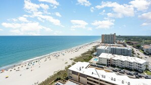 A beachside hotel with multiple buildings, a sandy beach, and a clear blue sky.