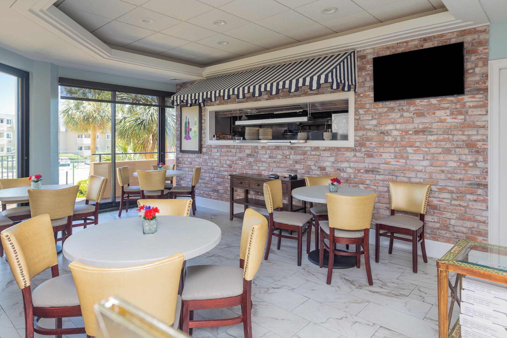 A restaurant with brick walls, a flat-screen TV, and round tables with cushioned chairs.