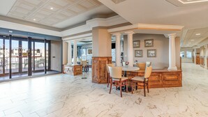 A spacious lobby with marble flooring, a central seating area with chairs and a table, and a view of the outside through large glass doors.