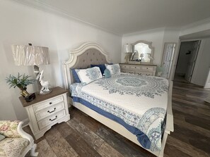 Ein Schlafzimmer mit einem großen Bett, einem Nachttisch, einer Kommode, einem Spiegel und einem Sessel.