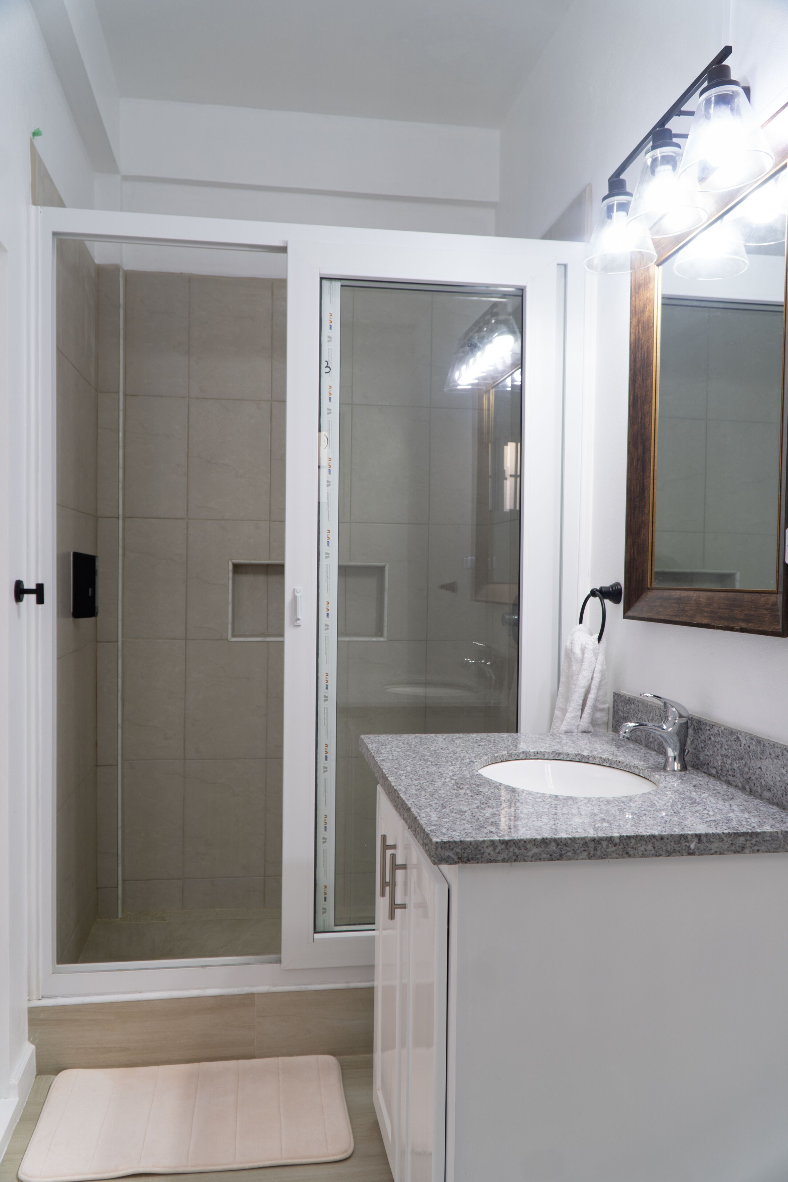 Une salle de bain moderne dotée d’une douche à parois de verre, d’un lavabo avec un plan de travail en granit et d’un miroir encadré en bois.