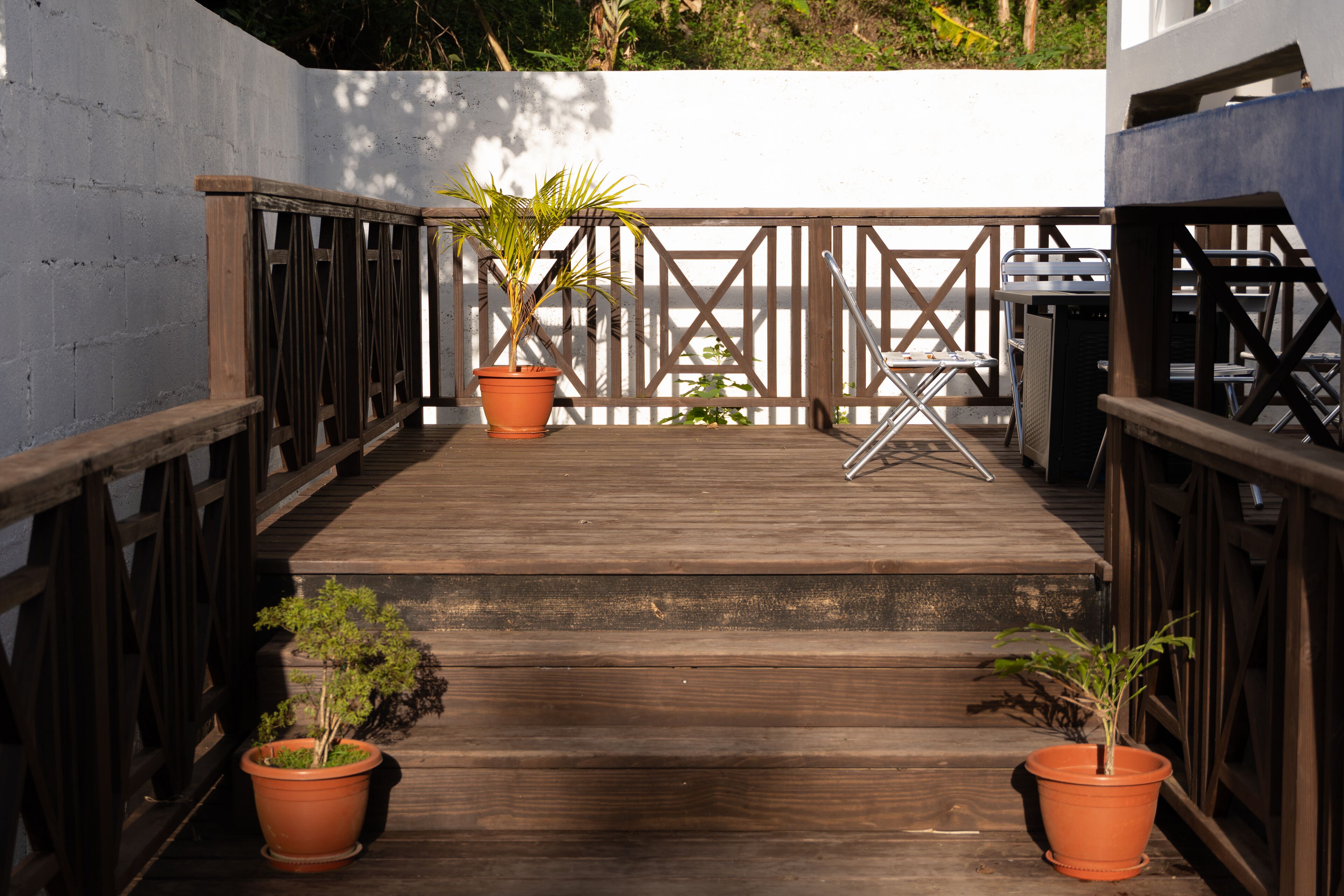A wooden deck with a railing, two potted plants, and a metal chair.