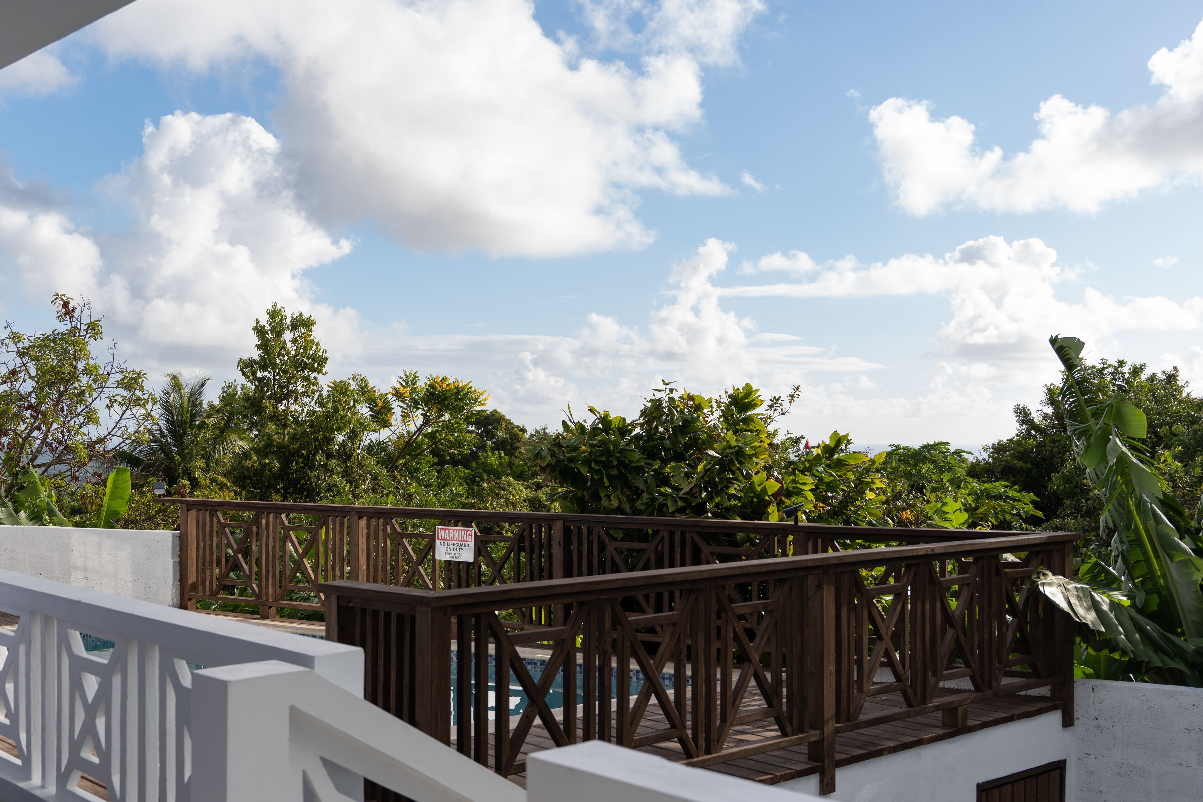 A wooden deck with a warning sign, surrounded by lush greenery and a clear sky.