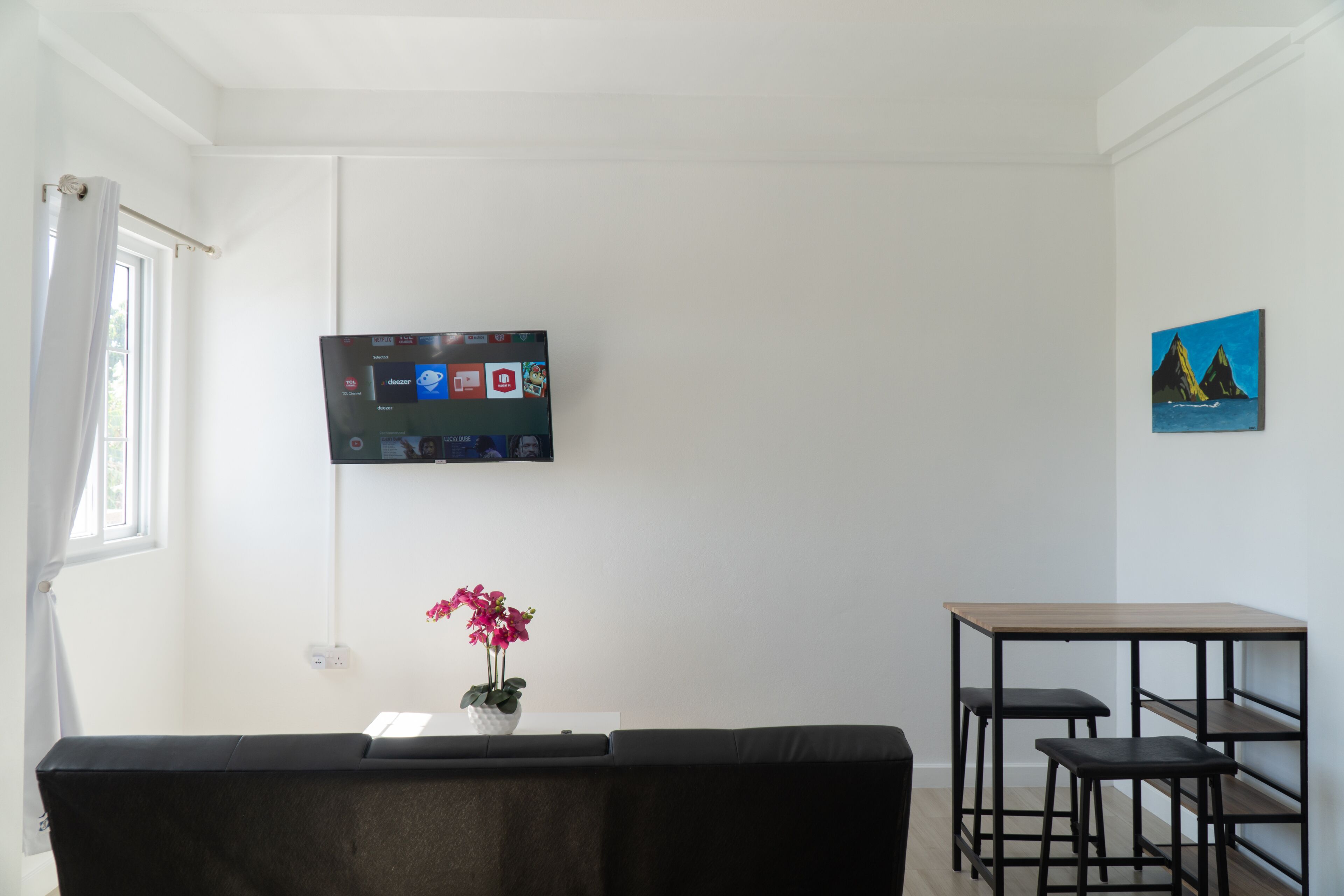 A living area with a black sofa, a small table, and a TV mounted on the wall.