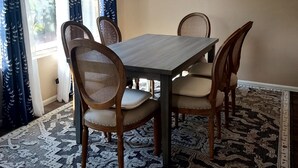 Comedor con mesa, sillas, candelabro, cuadro y alfombras estampadas.