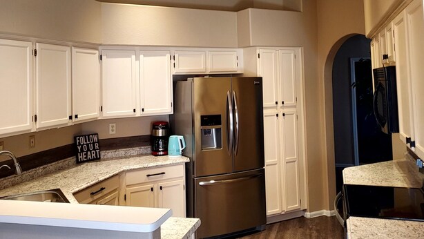 Cocina con armarios blancos, un refrigerador de acero inoxidable, una cafetera y un letrero que dice 'FOLLOW YOUR HEART'.