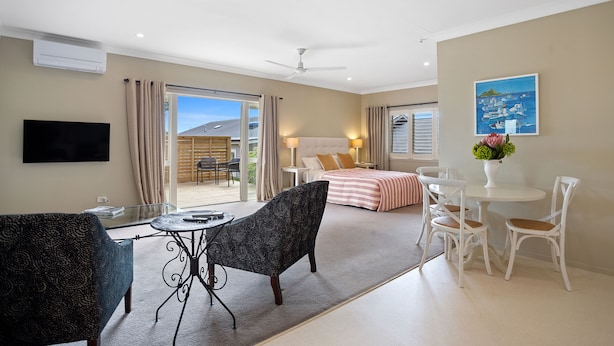 Une chambre d’hôtel moderne dotée d’un grand lit, d’un coin repas avec une table ronde et des chaises, d’un téléviseur fixé au mur et d’un balcon offrant une vue sur l’extérieur.