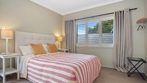 Une chambre à coucher avec un grand lit, deux tables de chevet, une fenêtre avec des rideaux et une petite table d’appoint.
