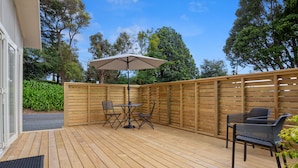 Une terrasse en bois avec une table et des chaises, un parasol et une clôture en bois.