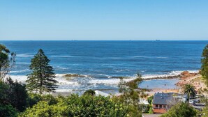 A coastal view with a beach, rocky shoreline, and a house with a red roof.