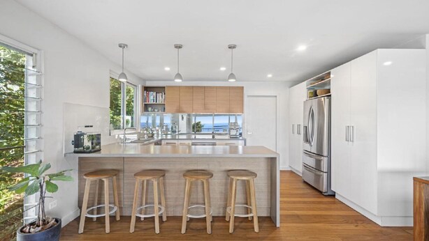 A modern kitchen with a central island, bar stools, stainless steel appliances, and a view to the outside.