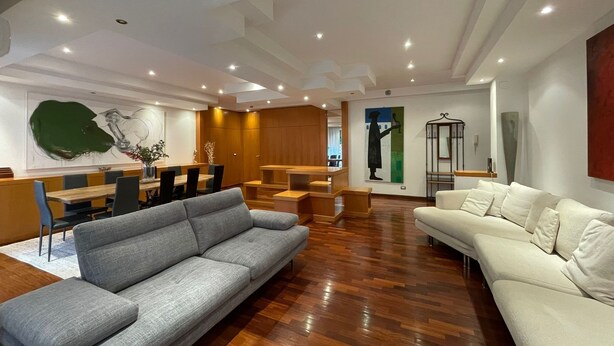 Ein modernes Wohnzimmer mit einem grauen Sofa, einem weißen Sofa, Holzboden und einem Essbereich mit einem Holztisch und Stühlen.