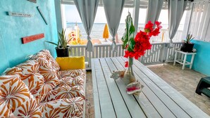 A room with a white ceiling, a blue wall, a white sofa with orange and white floral cushions, a white table with a vase of red flowers, and a view of the sea through large windows. - Amazing Ocean View Townhouse Condo Elevated Pool & Balcony (Nassau)