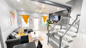 A modern living room with a black sofa, a dining table, and a staircase leading to an upper floor. - Amazing Ocean View Townhouse Condo Elevated Pool & Balcony (Nassau)