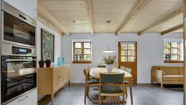 A modern kitchen with a built-in oven, wooden cabinets, and a dining area with a round table and chairs.