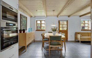 Uma cozinha moderna com forno embutido, armários de madeira e um espaço de refeições com mesa e cadeiras redondas.