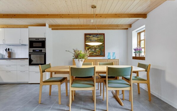 Uma cozinha moderna com armários brancos, forno embutido e área de jantar com mesa de madeira e cadeiras verdes.