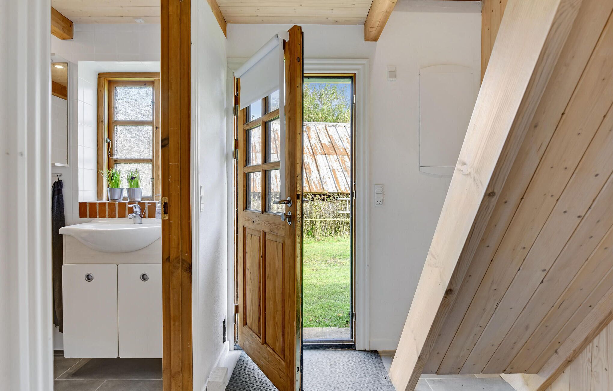 A bathroom with a sink, mirror, and wooden door leading to a garden.