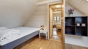 A cozy attic bedroom with a bed, a small table, and a wooden door leading to a bathroom.