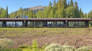 Un bâtiment moderne doté d’une longue façade continue en verre, intégré dans un paysage naturel avec une montagne en arrière-plan.