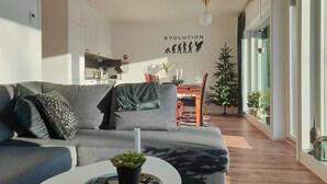 Un salon moderne avec un canapé gris, une petite table sur laquelle est posée une plante, et une œuvre d’art murale représentant l’évolution.