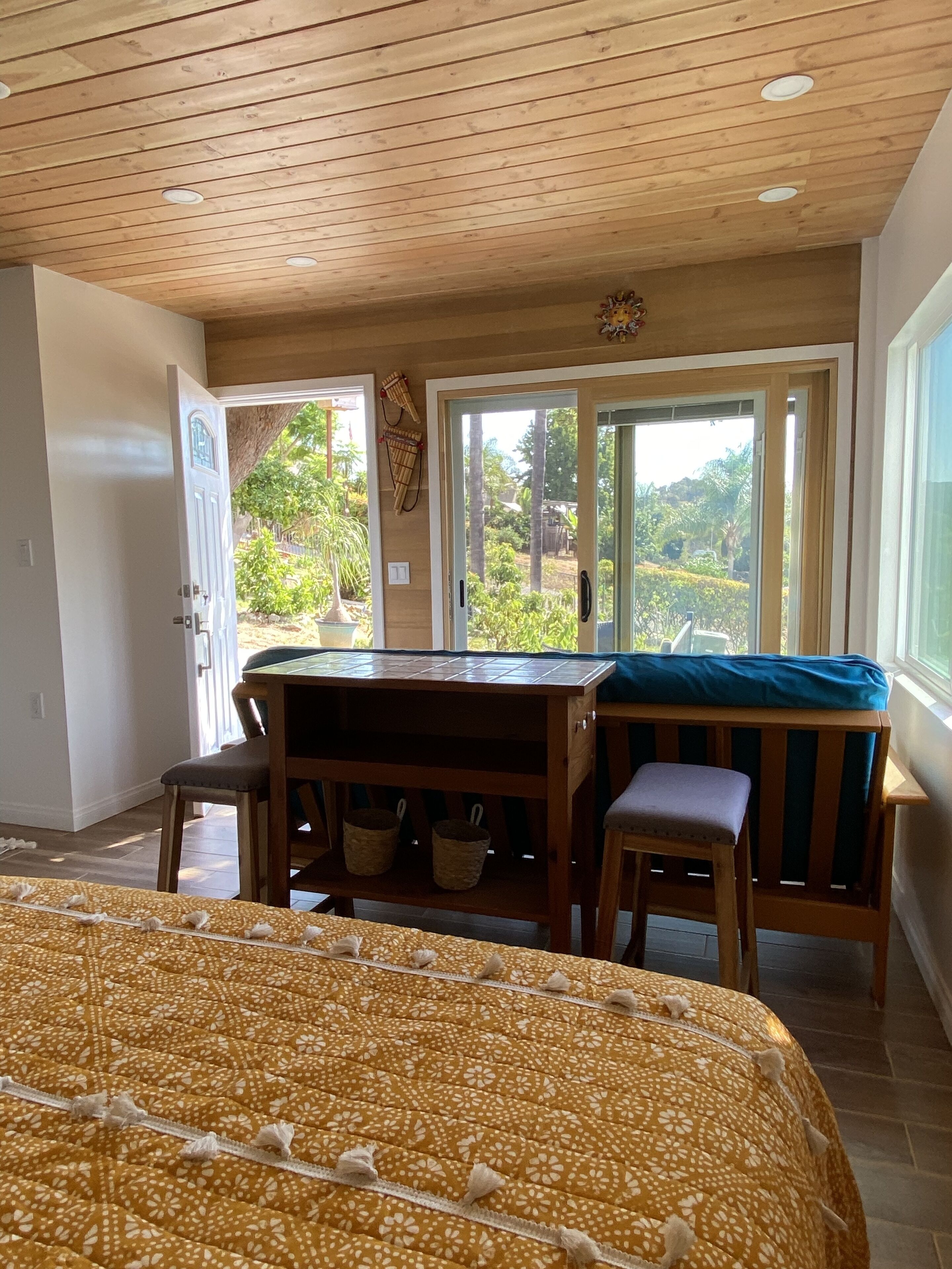 Ein Zimmer mit einem Bett, einem Holztisch mit einer Bank und Blick auf Grünfläche.