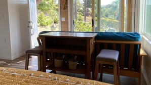 Une pièce avec un lit, une table en bois et un banc, et une vue sur la verdure à l’extérieur.